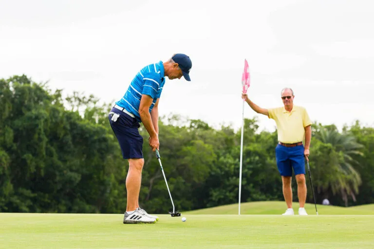 Golfer holding flag while player putts